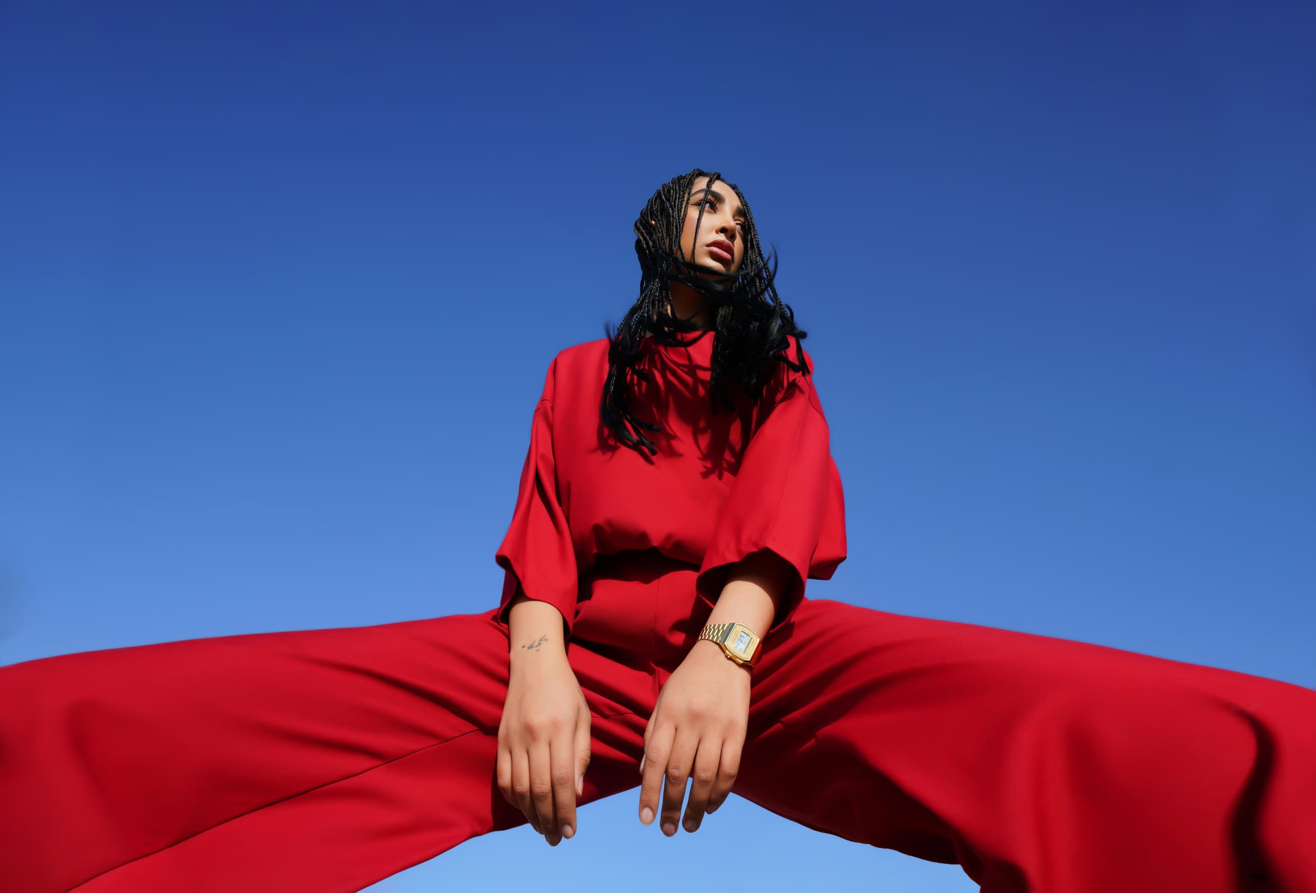 Model in bold red trend-led outfit against a clear blue sky, campaign photography